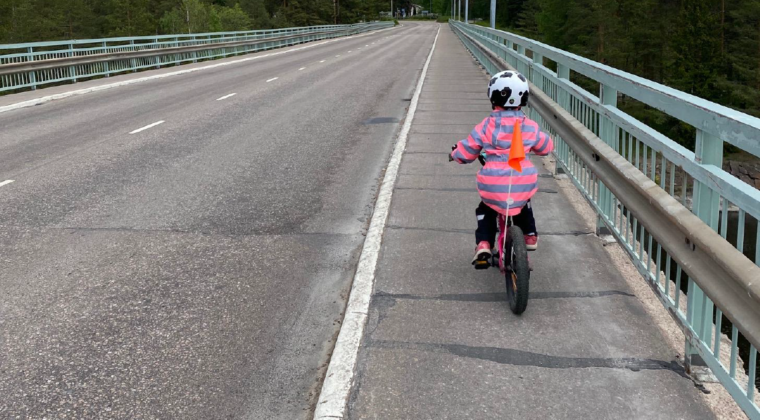 PIeni lapsi pyöräilemässä vaaleanpunaisessa takissa Keskikosken sillan kevyen liikenteen väylällä.
