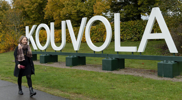 Nainen kävelee Kouvola-kirjainten ohi ruska-aikaan.