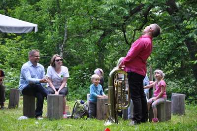 Eri ikäisiä ihmisiä kuuntelamassa esiintyjään puulajipuistossa Mustila Arboretumissa