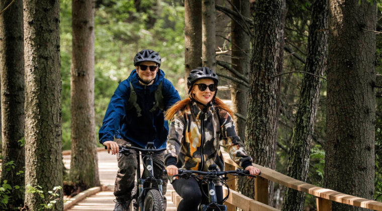 Kaksi maastopyöräilijää ajaa rakennetulla puisella polulla metsässä.