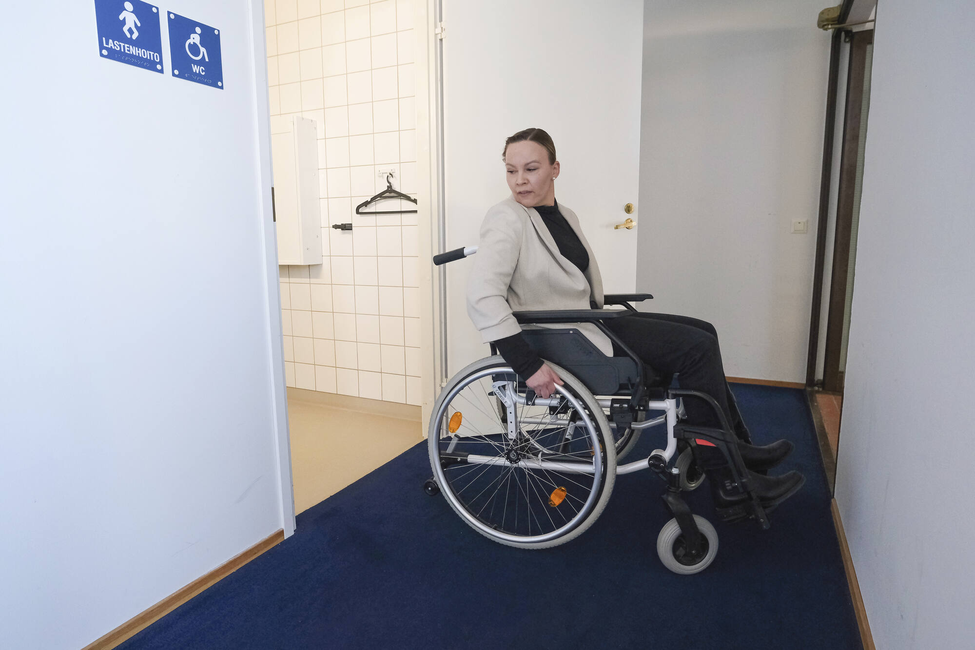 Nainen pyörätuolissa tulossa tai menossa wc-tiloihin.