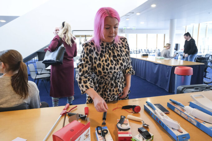 Pinkki-hiuksinen nainen katselee pöydällä olevia apuvälineitä, kuten tukevartista lusikkaa.