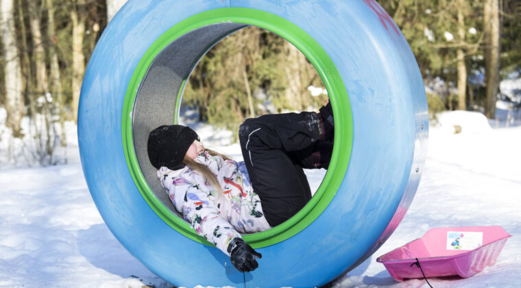 Lapsi makaa ison sinisen renkaan sisällä leikkipuistossa.