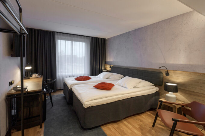 Hotel room with a double bed, wood-patterned floors, wooden furniture and half-wall wood panelling, as well as dark curtains and upholstery.