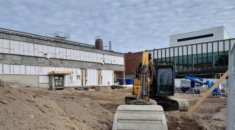 Kouvolan uuden teatterin rakennustyömaa. Edessä näkyy kauhakuormaaja ja hiekkaa, taustalla nykyinen teatteri sekä kuntotalo, jota saneeratan.