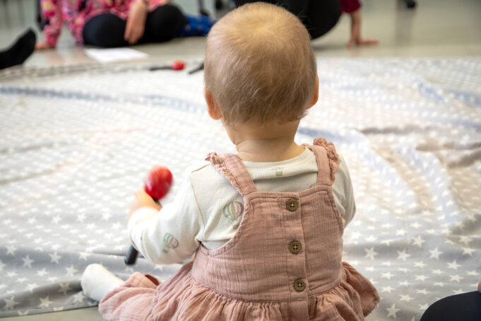 A baby is sitting on the floor with a maracas in her hand.