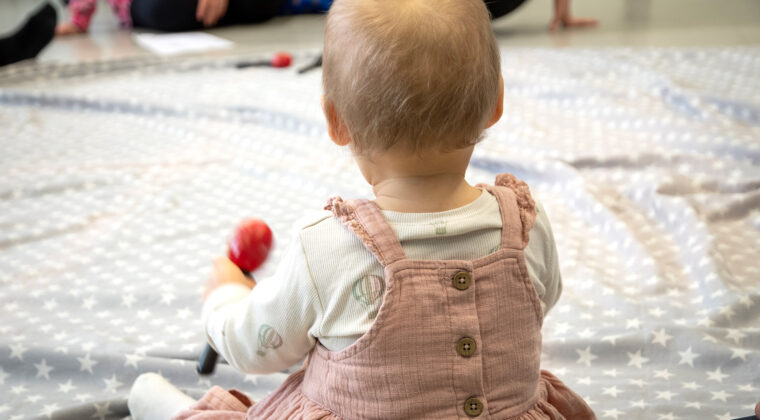 Vauva istuu lattialla marakassi kädessään.