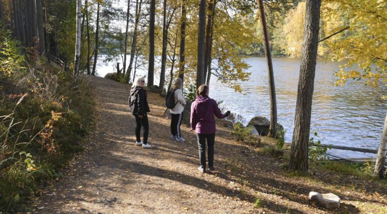 Kolme henkilöä kävelemässä ulkoilureitillä syksyisessä maastossa.