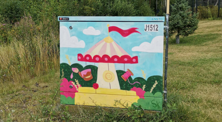 Kirkkain värein maalattu sähkökaappi nurmialueella. Maalauksen aiheena on karuselli.
