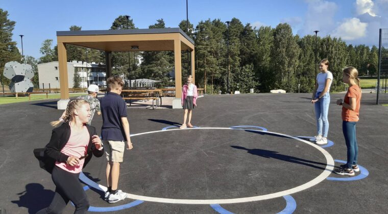 Lapset leikkivät tervapataa asfalttipihalla. Yksi henkilö juoksee parhaillaa rinkiä ympäri.