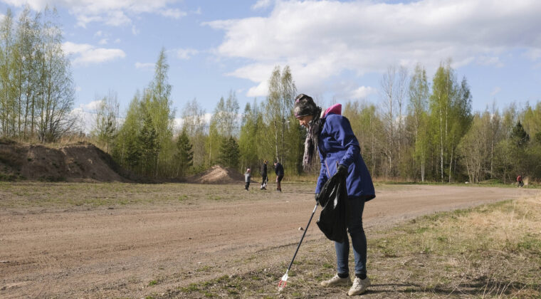 Henkilö kerää roskia hiekkakentällä. Taustalla muita kerääjiä. On kevät.