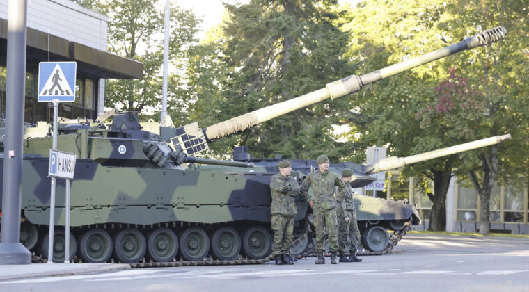 Kaksi Puolustusvoimien panssarivauhut, joiden edessä on muutamia sotilashenkilöitä.