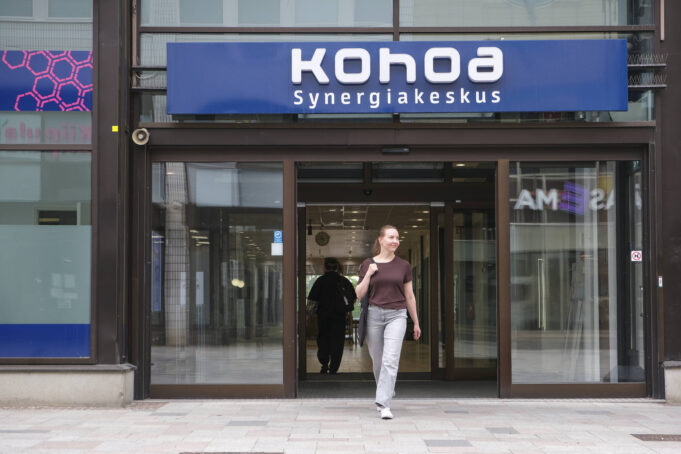Nainen kävelee ulos Kohoa Synergiakeskus -rakennuksen liukuovista.