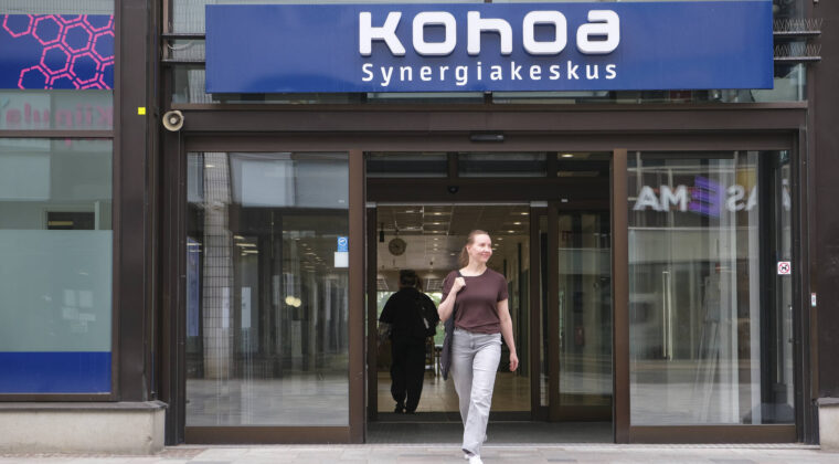 Nainen kävelee ulos Kohoa Synergiakeskus -rakennuksen liukuovista.